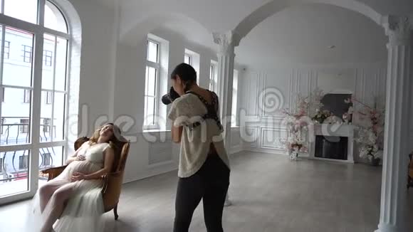 美丽的年轻孕妇坐在白色的椅子上向摄影师摆姿势视频的预览图
