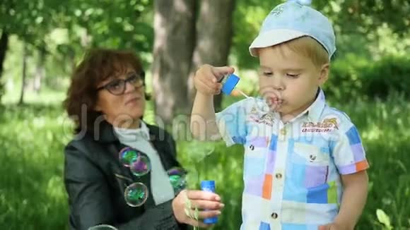 祖母带着一个孩子在公园里玩耍充气肥皂泡户外娱乐视频的预览图