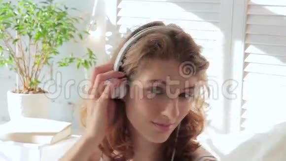 美丽的年轻女子一边看着摄像机一边听着耳机上的音乐视频的预览图