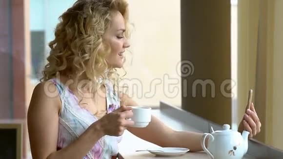 年轻女子在午休时坐在咖啡馆里在智能手机数码相机上做自我画像视频的预览图