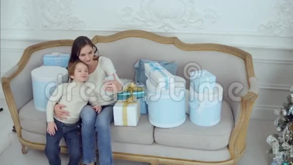 年轻的母亲和快乐的儿子被圣诞礼物包围带着手机自拍视频的预览图