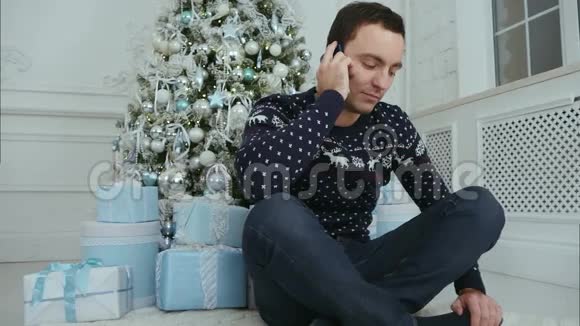 坐在圣诞树下打电话的年轻人视频的预览图