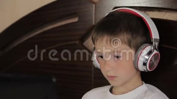 这个男孩躺在床上听音乐或者用他的平板电脑上一节电子学习课它连接着一对视频的预览图
