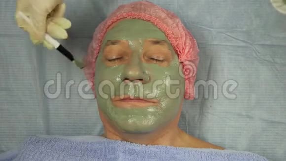 戴手套的女性美容师给男性客户戴上带刷子的口罩视频的预览图