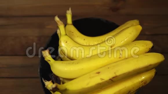 熟湿的香蕉在木桌上的黑色盘子上旋转视频的预览图