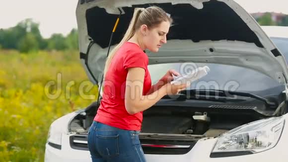 惹怒了年轻女子她看着汽车手册试图在荒芜的道路上修理破车视频的预览图