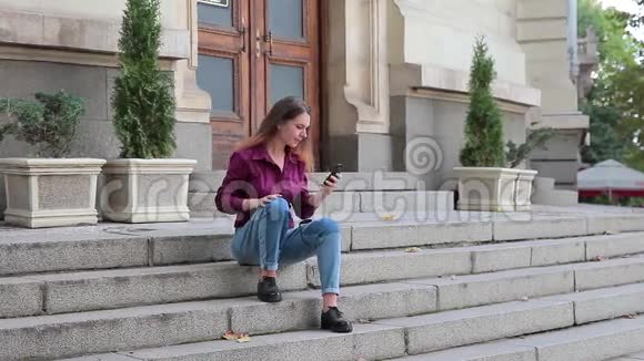 年轻的休闲女士坐在大楼的台阶上用手机自拍视频的预览图