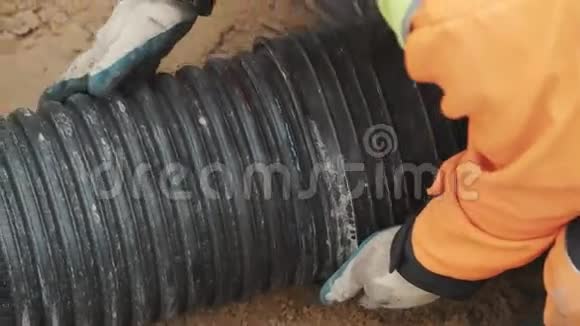 戴橙色安全帽和手套的工人把塑料黑管放在沙子表面视频的预览图