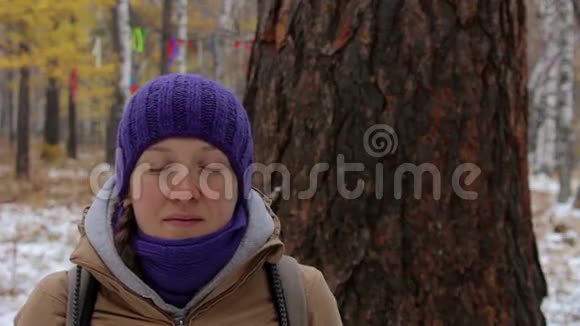年轻女子在冬林中的老大树附近冥想特写视频的预览图