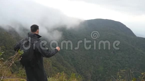 年轻的男性徒步旅行者背包伸向山顶举起双手站在边缘的观光客视频的预览图