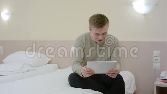 年轻人刚来到酒店房间坐在床上在平板电脑上视频聊天视频的预览图