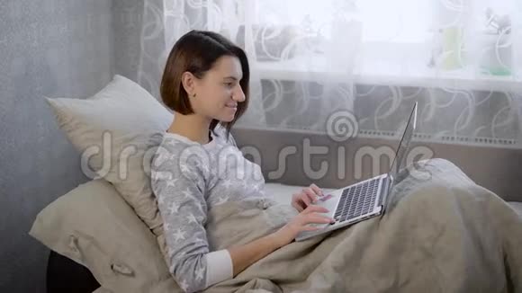 房间里床上的女孩黑发女人半坐在床上女人检查笔记本电脑上的信息反对视频的预览图