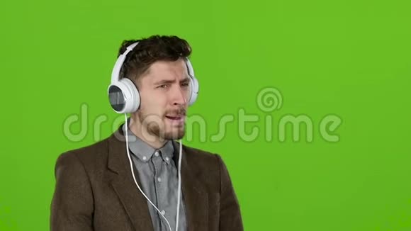 男人通过耳机听音乐跳舞和唱歌绿色屏幕慢动作视频的预览图