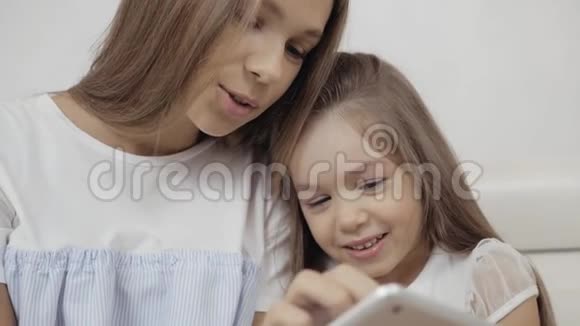 两个姐姐看着平板电脑坐在沙发上玩游戏小婴儿和成年妹妹视频的预览图