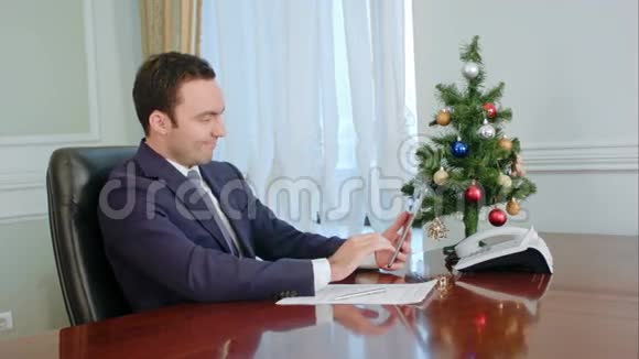 年轻的商人用平板电脑打电话微笑着祝贺圣诞节视频的预览图