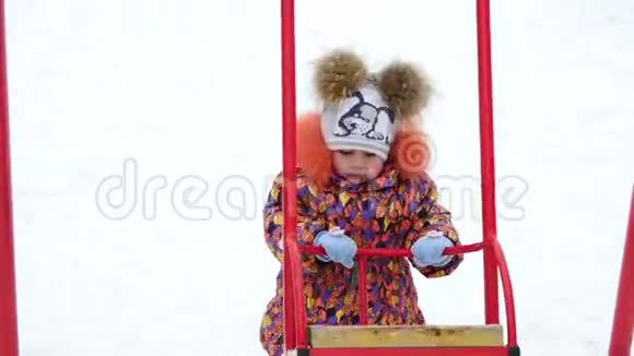 可爱的小女孩在冬天的公园里玩秋千视频的预览图