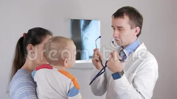 一位年轻的男医生用听诊器给孩子玩这个男孩在他母亲怀里视频的预览图