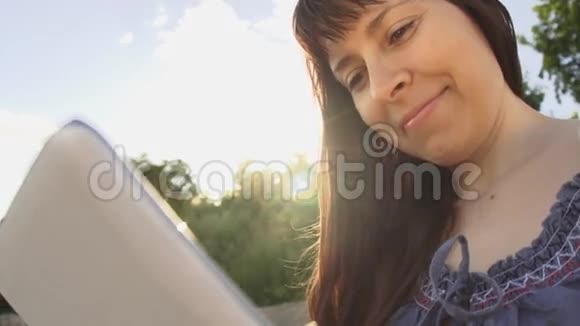 在日落特写镜头下一个拿着平板电脑的女人在草地旁边视频的预览图