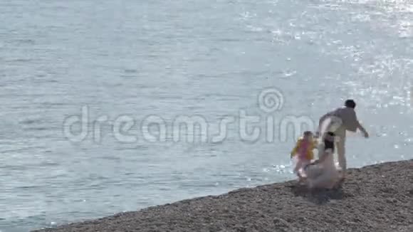 快乐的父母和女儿在阳光明媚的日子里走在海岸上视频的预览图