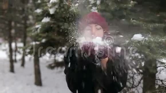 年轻漂亮的女人在冬天的背景下对着镜头吹雪视频的预览图