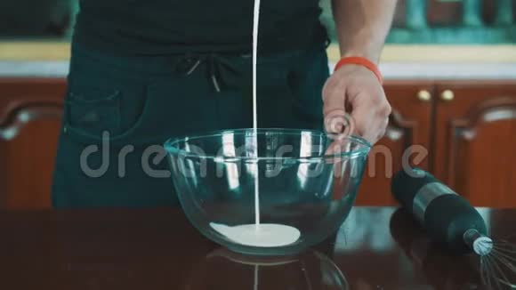 男性厨师用搅拌器将牛奶倒入厨房桌子上的玻璃碗中视频的预览图