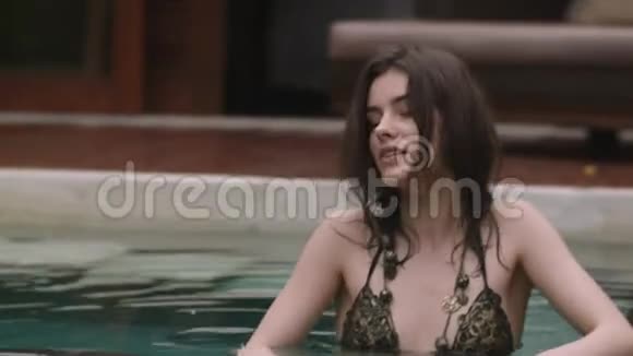 在热带度假胜地的游泳池里一位头发湿漉漉的年轻女子尽情放松视频的预览图