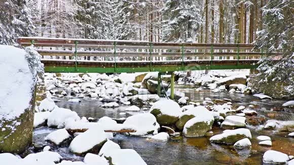 早晨在冬天的森林里下雪旅游路线在森林冻结的河流上的木桥视频的预览图