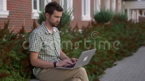 穿着休闲服的男人戴着智能手表坐在长凳上用笔记本电脑聊天视频的预览图