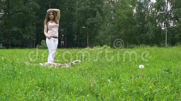 一位年轻的美女站在公园草地上的格子呢上视频的预览图