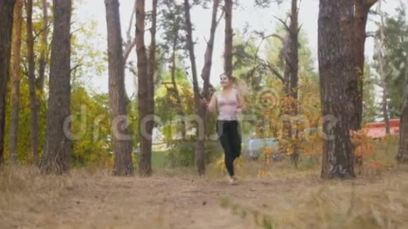 美丽的微笑女人用自拍棒制作视频她在森林里奔跑视频的预览图