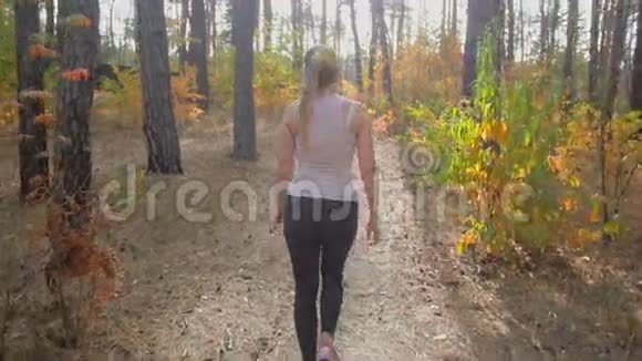后景拍摄的美丽苗条的女士穿着运动服在森林里散步视频的预览图