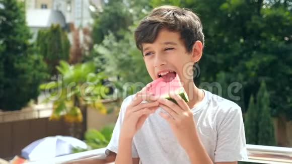 男孩少年在外面吃西瓜背景是绿色和天空慢动作视频的预览图