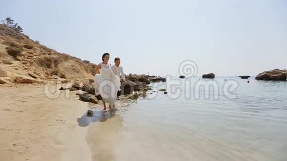 成年男性新郎和女性新娘赤脚在海滩上奔跑视频的预览图