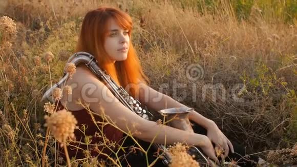 夕阳西下的剪影年轻漂亮的红发女孩在玩萨克斯管自然一个女人吹进烟斗概念爱好音乐视频的预览图