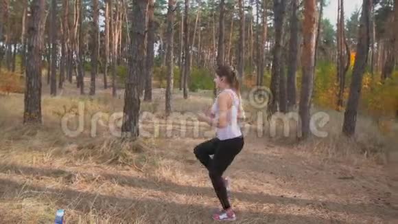 年轻苗条的女人跑步前在森林里热身的慢镜头视频的预览图