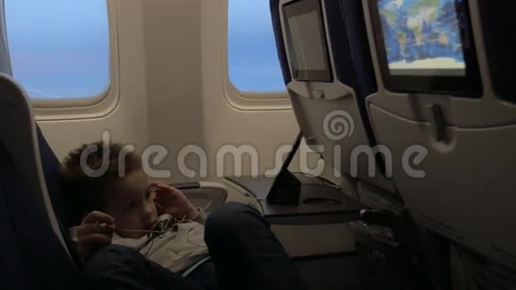 小男孩坐在飞机靠窗的座位上用耳机看电影视频的预览图