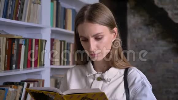 年轻严肃的女孩正在看书在镜头前看书在后台看图书馆视频的预览图