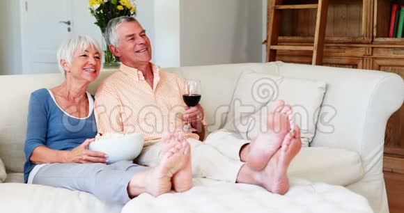 高级夫妇在客厅里吃爆米花和一杯葡萄酒视频的预览图