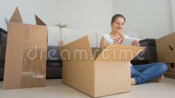 年轻女子在收拾东西搬到新公寓时使用数码平板电脑的多利镜头视频的预览图