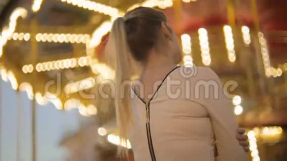 后景拍摄的优雅女人穿着衣服看着明亮的旋转木马在公园视频的预览图