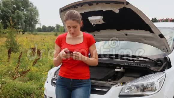 年轻的担心的女人站在破车旁边在现场打电话视频的预览图
