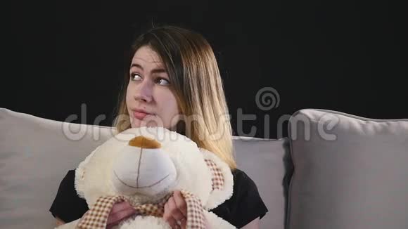 坐在沙发上抱着玩具熊的漂亮微笑的女人视频的预览图