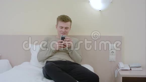 英俊的年轻人在家里的卧室里用智能手机笑视频的预览图