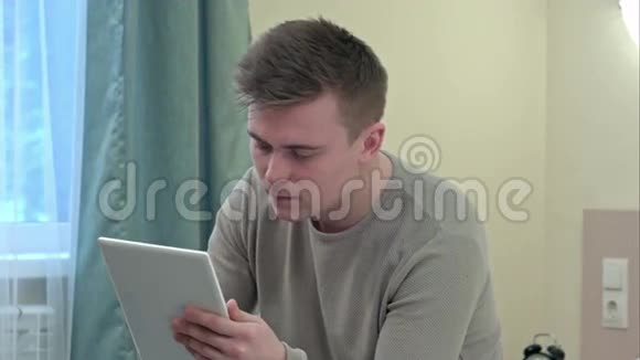 担心的商人穿着休闲服装用他的数字平板电脑读床新闻打电话视频的预览图