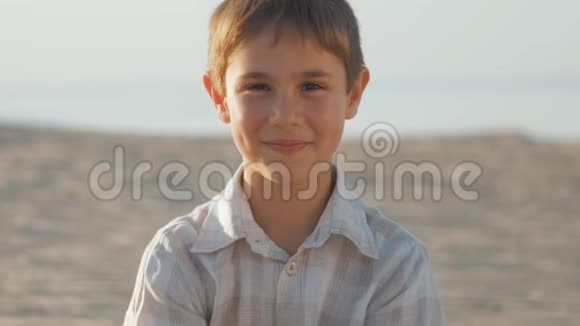 一个10岁的男孩穿着白色衬衫在一个夏天海滩的背景上的肖像视频的预览图