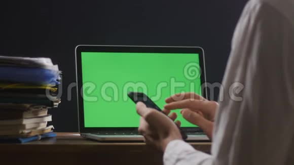 人类正在使用智能手机他的笔记本电脑上有一个绿色屏幕或一个色度在他的桌面上商人在这里工作视频的预览图