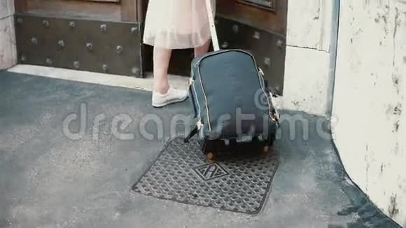 年轻的旅行者女人带着手提箱在街上散步女孩打开门走进拱门视频的预览图