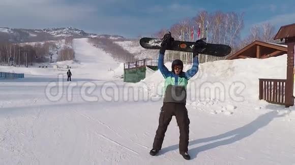 快乐的男性滑雪者手里拿着滑雪板站在滑雪场上快乐地跳舞穿着冬装的男人视频的预览图