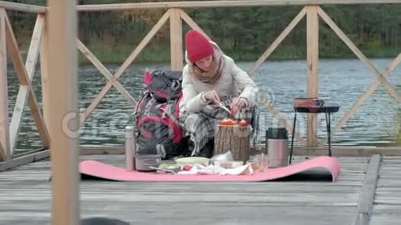 一位穿着暖和衣服的女游客背着背包在河边的一座桥上筛蔬菜准备食物视频的预览图