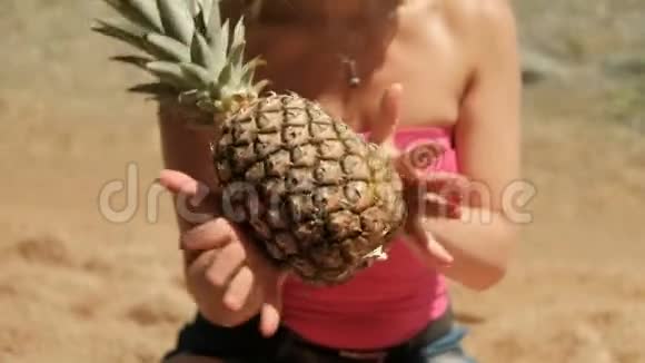 穿着粉红色T恤的女人在海滩上滚动菠萝水果视频的预览图
